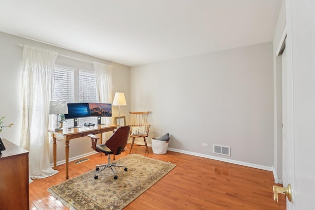 office space with baseboards, visible vents, and wood finished floors