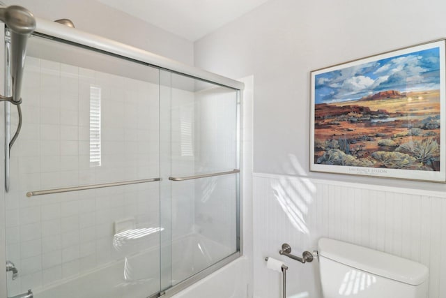 bathroom featuring enclosed tub / shower combo, a wainscoted wall, and toilet