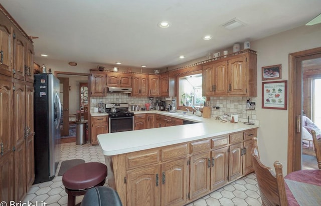 kitchen featuring visible vents, appliances with stainless steel finishes, a peninsula, light countertops, and under cabinet range hood