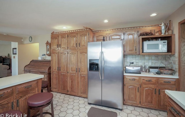 kitchen featuring brown cabinets, light countertops, stainless steel refrigerator with ice dispenser, and white microwave