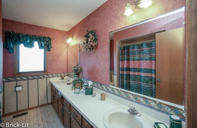 full bathroom with tile patterned floors, a sink, a shower with curtain, double vanity, and wallpapered walls