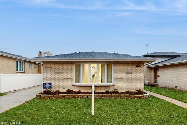 view of front of property with roof with shingles, fence, a front lawn, and brick siding