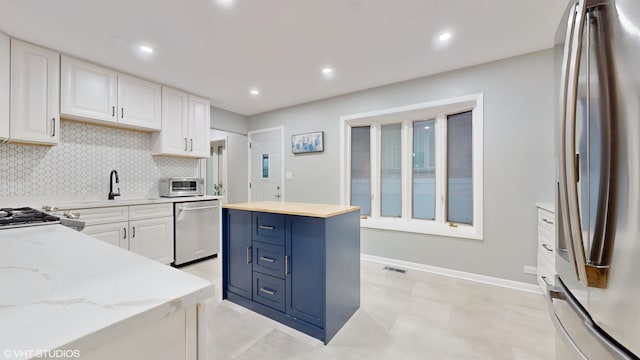 kitchen featuring stainless steel appliances, a sink, visible vents, white cabinetry, and backsplash