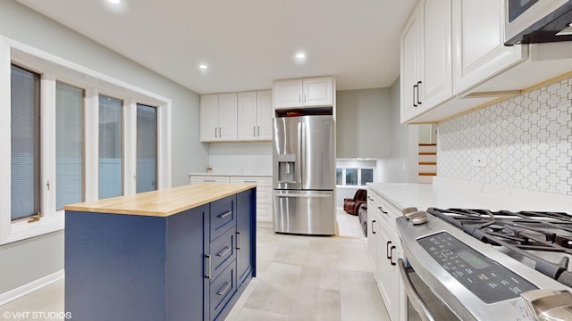 kitchen featuring blue cabinets, stainless steel appliances, white cabinetry, wooden counters, and tasteful backsplash