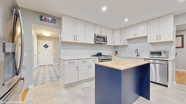 kitchen featuring wooden counters, appliances with stainless steel finishes, a sink, and white cabinetry