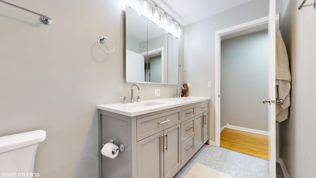 full bath featuring toilet, double vanity, baseboards, and a sink