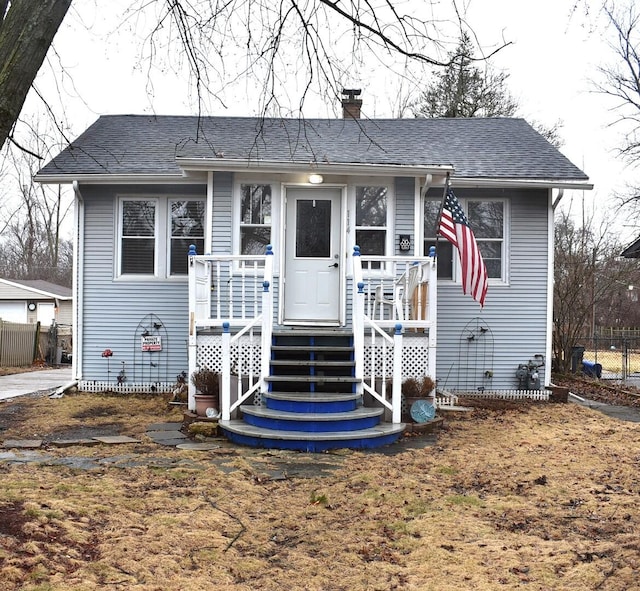 bungalow with a shingled roof, a chimney, and fence