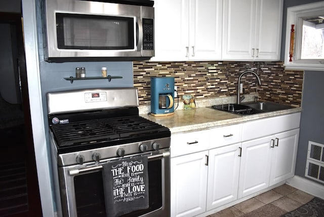 kitchen with appliances with stainless steel finishes, backsplash, a sink, and white cabinetry