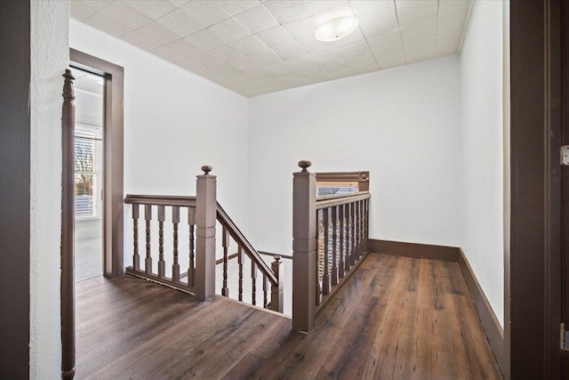 hallway with baseboards, wood finished floors, and an upstairs landing