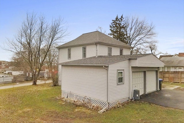 view of side of property with driveway, a shingled roof, an attached garage, fence, and a yard