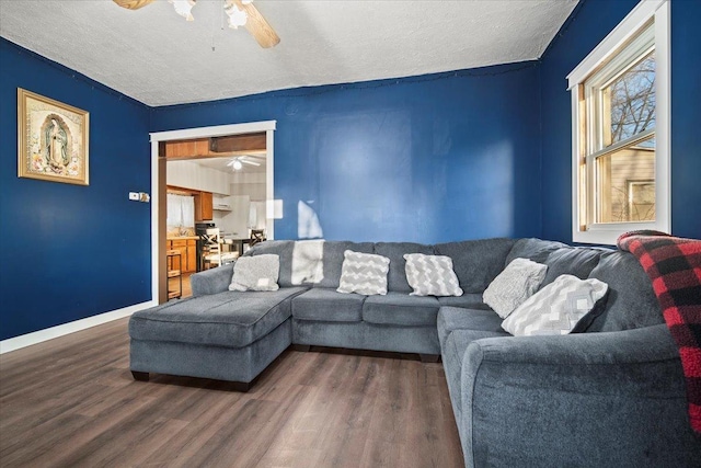 living room featuring a textured ceiling, baseboards, dark wood finished floors, and a ceiling fan