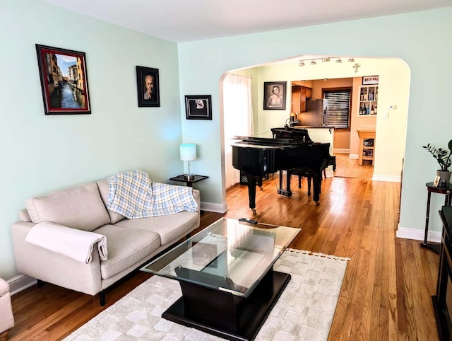 living area with baseboards, arched walkways, and wood finished floors