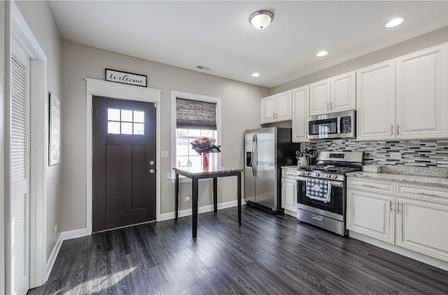 kitchen with white cabinetry, dark hardwood / wood-style flooring, light stone counters, appliances with stainless steel finishes, and decorative backsplash