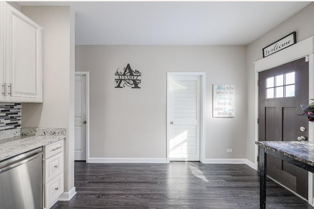 kitchen with light stone counters, white cabinetry, dark wood-type flooring, stainless steel dishwasher, and decorative backsplash