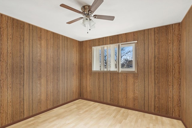 empty room with ceiling fan, light wood-type flooring, and wooden walls