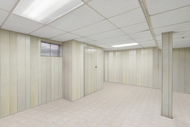 basement featuring a paneled ceiling and wooden walls