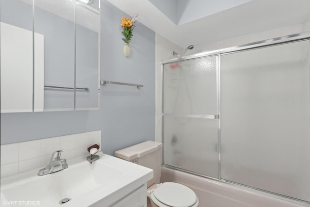 full bathroom featuring bath / shower combo with glass door, vanity, toilet, and tasteful backsplash