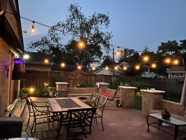 patio terrace at dusk with outdoor dining space and a fenced backyard