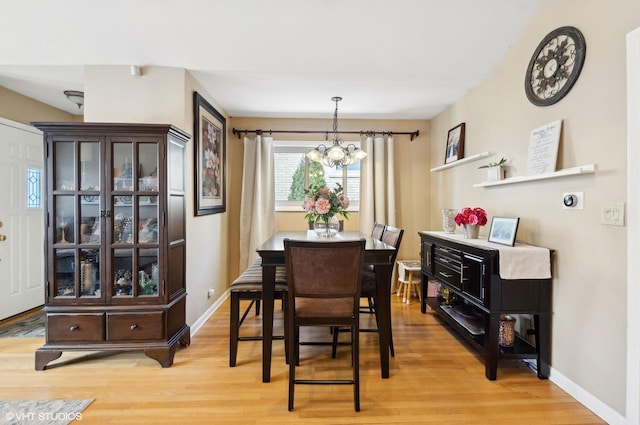 dining area featuring a chandelier, baseboards, and light wood finished floors