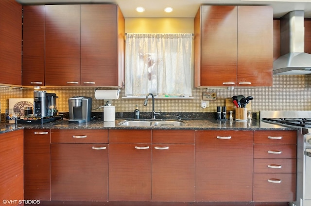 kitchen featuring stainless steel range oven, wall chimney exhaust hood, dark stone countertops, and a sink