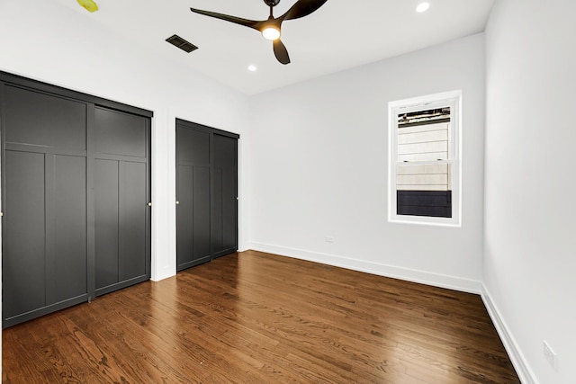 unfurnished bedroom featuring baseboards, a ceiling fan, dark wood-type flooring, two closets, and recessed lighting