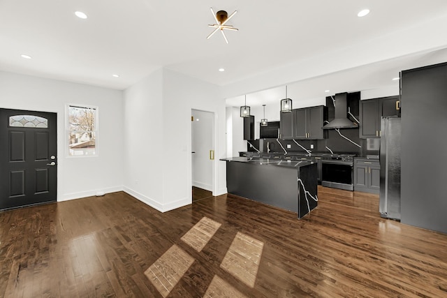 kitchen featuring stainless steel appliances, a kitchen breakfast bar, wall chimney exhaust hood, an island with sink, and pendant lighting