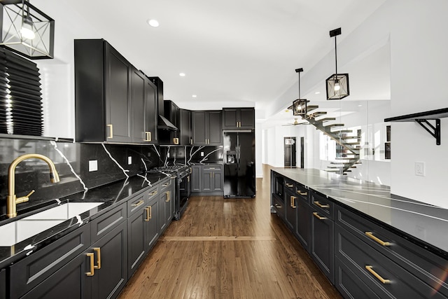 kitchen with dark cabinets, a sink, hanging light fixtures, black fridge, and dark wood finished floors