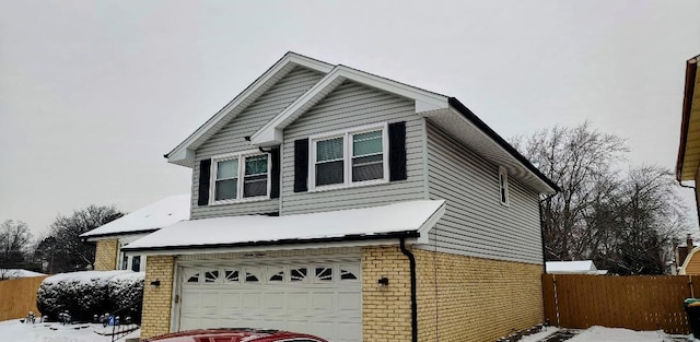 view of front facade with a garage, fence, brick siding, and driveway