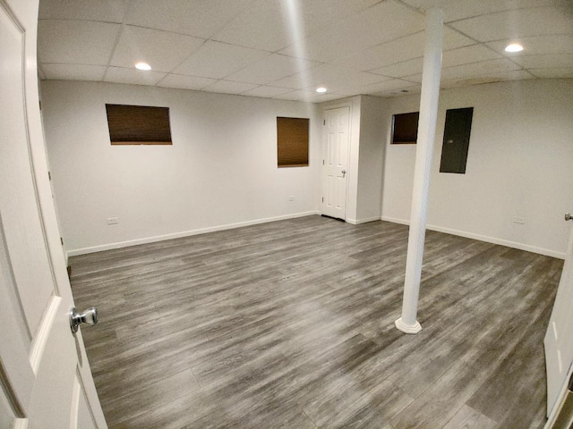 finished basement featuring electric panel, dark wood-style floors, baseboards, and a paneled ceiling