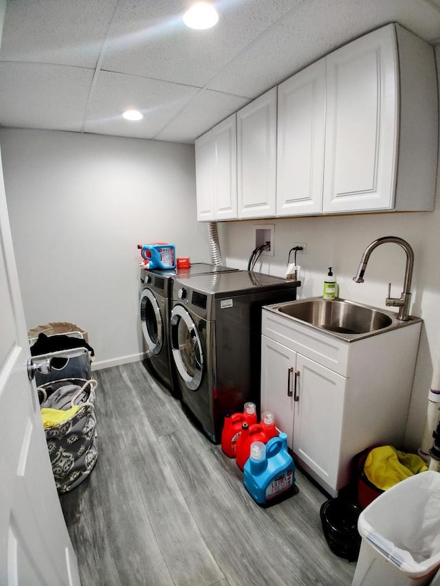 clothes washing area featuring a sink, wood finished floors, cabinet space, baseboards, and washing machine and clothes dryer