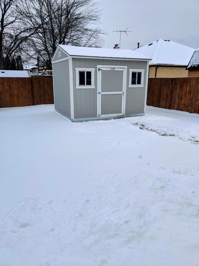 snow covered structure featuring a storage unit, a fenced backyard, and an outdoor structure