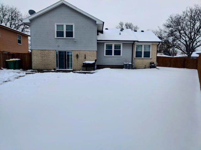 snow covered rear of property featuring brick siding, cooling unit, and fence