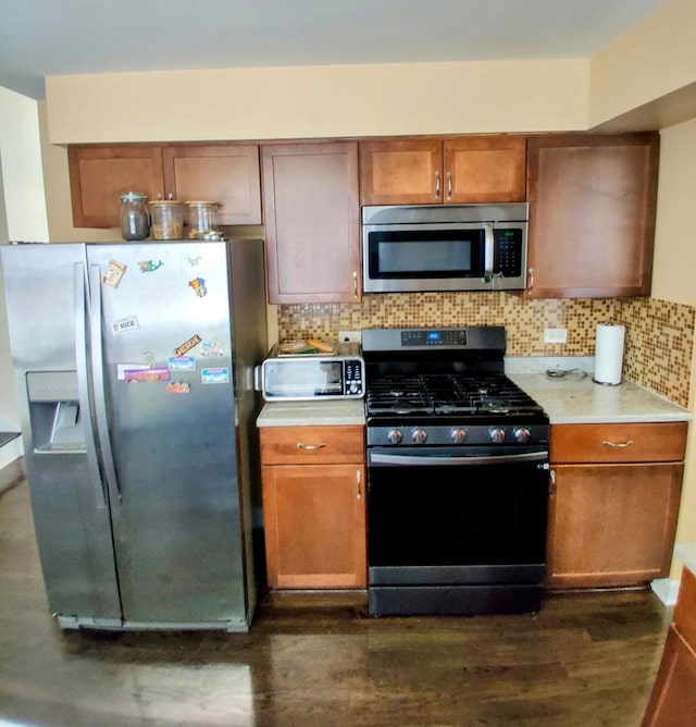 kitchen with tasteful backsplash, dark wood finished floors, light countertops, brown cabinets, and appliances with stainless steel finishes