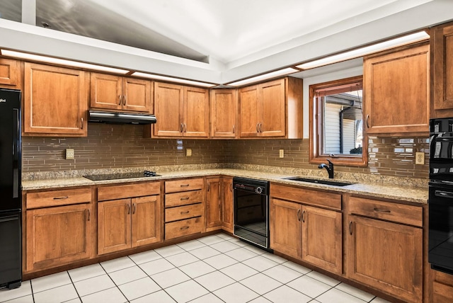 kitchen with brown cabinets, black appliances, under cabinet range hood, a sink, and vaulted ceiling