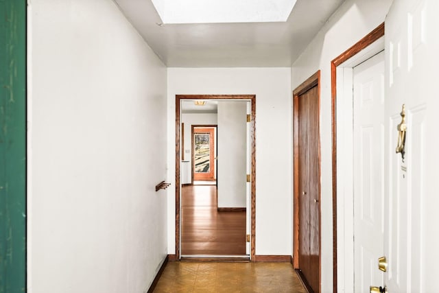 hallway with baseboards, a skylight, and dark floors