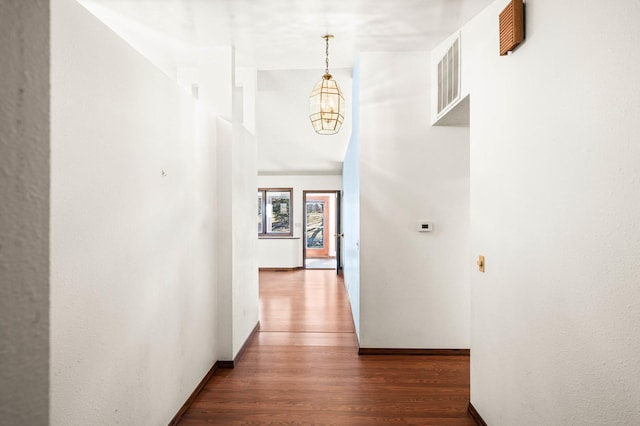 hallway featuring visible vents, baseboards, wood finished floors, a towering ceiling, and an inviting chandelier