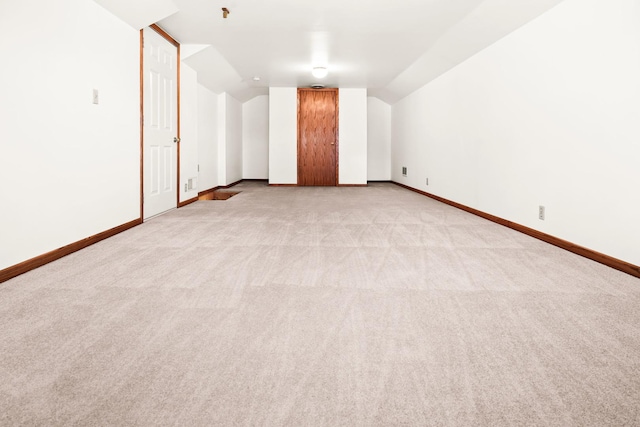 interior space with vaulted ceiling, baseboards, and light carpet