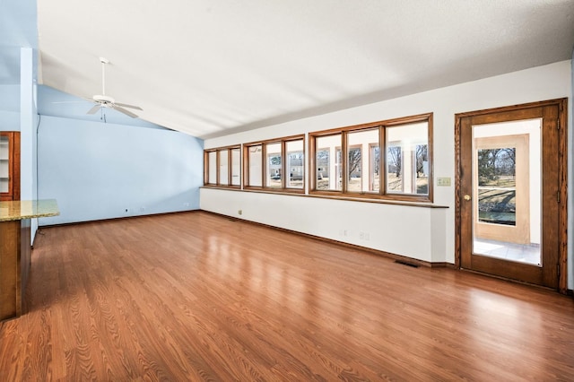 unfurnished living room with a ceiling fan, lofted ceiling, wood finished floors, and baseboards