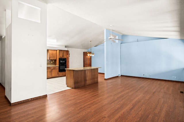 kitchen with light wood-type flooring, ceiling fan with notable chandelier, a kitchen island, brown cabinetry, and light countertops