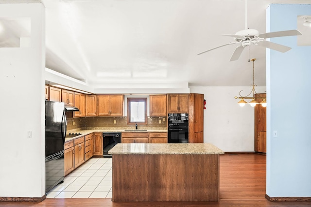 kitchen featuring a sink, decorative backsplash, black appliances, under cabinet range hood, and a center island