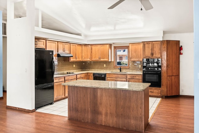 kitchen featuring under cabinet range hood, black appliances, tasteful backsplash, and a sink