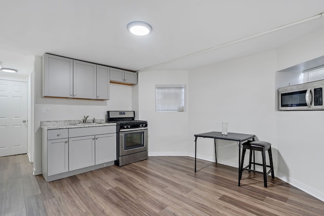 kitchen with appliances with stainless steel finishes, light wood-type flooring, gray cabinetry, and a sink