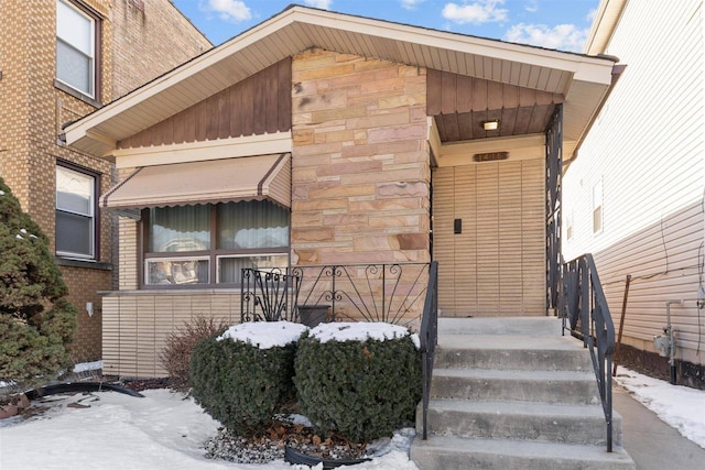 snow covered property entrance featuring stone siding and brick siding