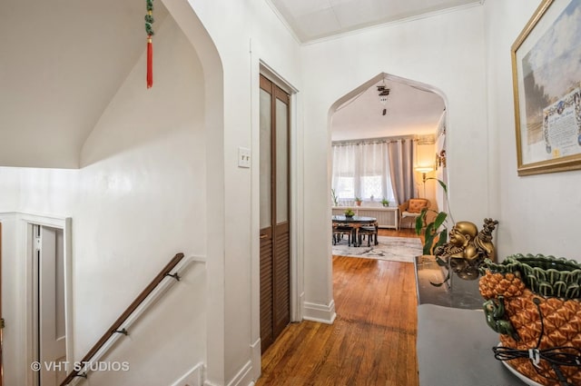 corridor featuring arched walkways, wood finished floors, an upstairs landing, and crown molding