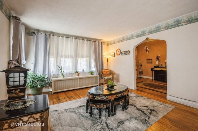 living area featuring arched walkways, radiator, a textured ceiling, wood finished floors, and baseboards