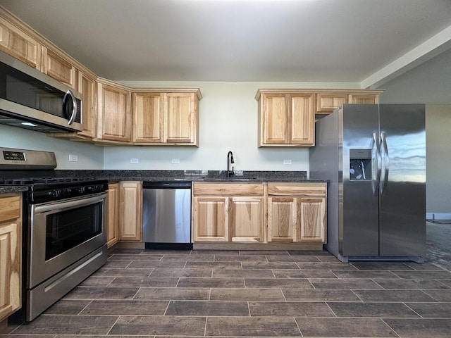 kitchen with light brown cabinetry, stainless steel appliances, a sink, and wood finish floors