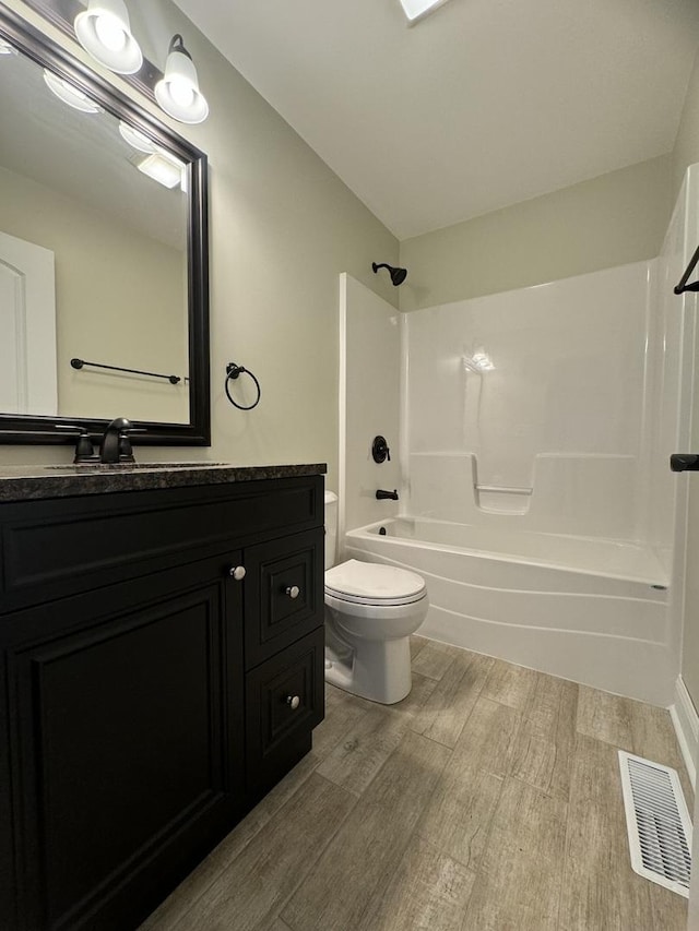 bathroom with visible vents, toilet, wood finished floors,  shower combination, and vanity