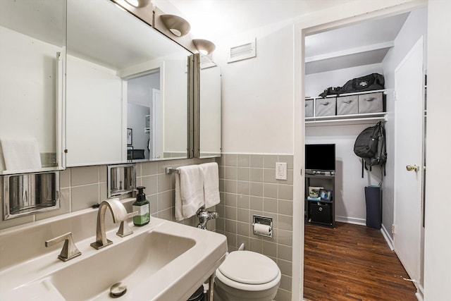 half bathroom featuring toilet, wood finished floors, a sink, and tile walls