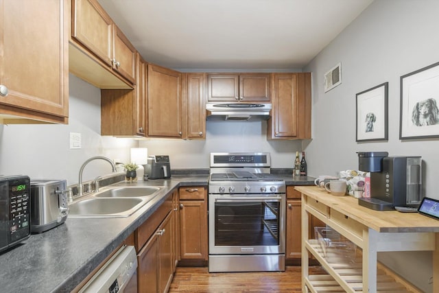 kitchen featuring under cabinet range hood, a sink, appliances with stainless steel finishes, brown cabinetry, and dark countertops