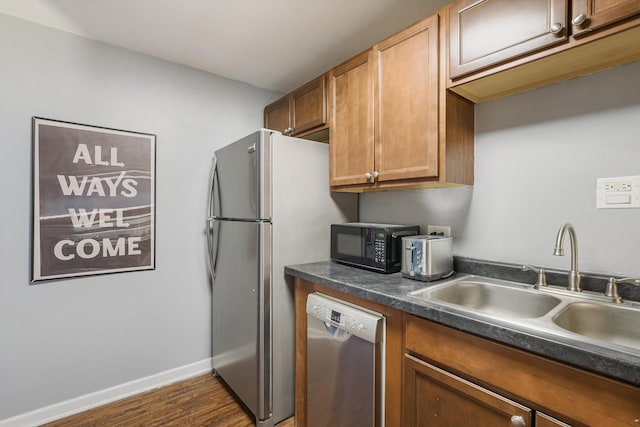 kitchen with baseboards, dark countertops, brown cabinets, stainless steel appliances, and a sink